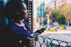 Woman looking through the window holding a cup of coffee and a cellphone