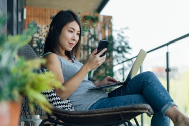 Woman in a chair looking at her phone and laptop